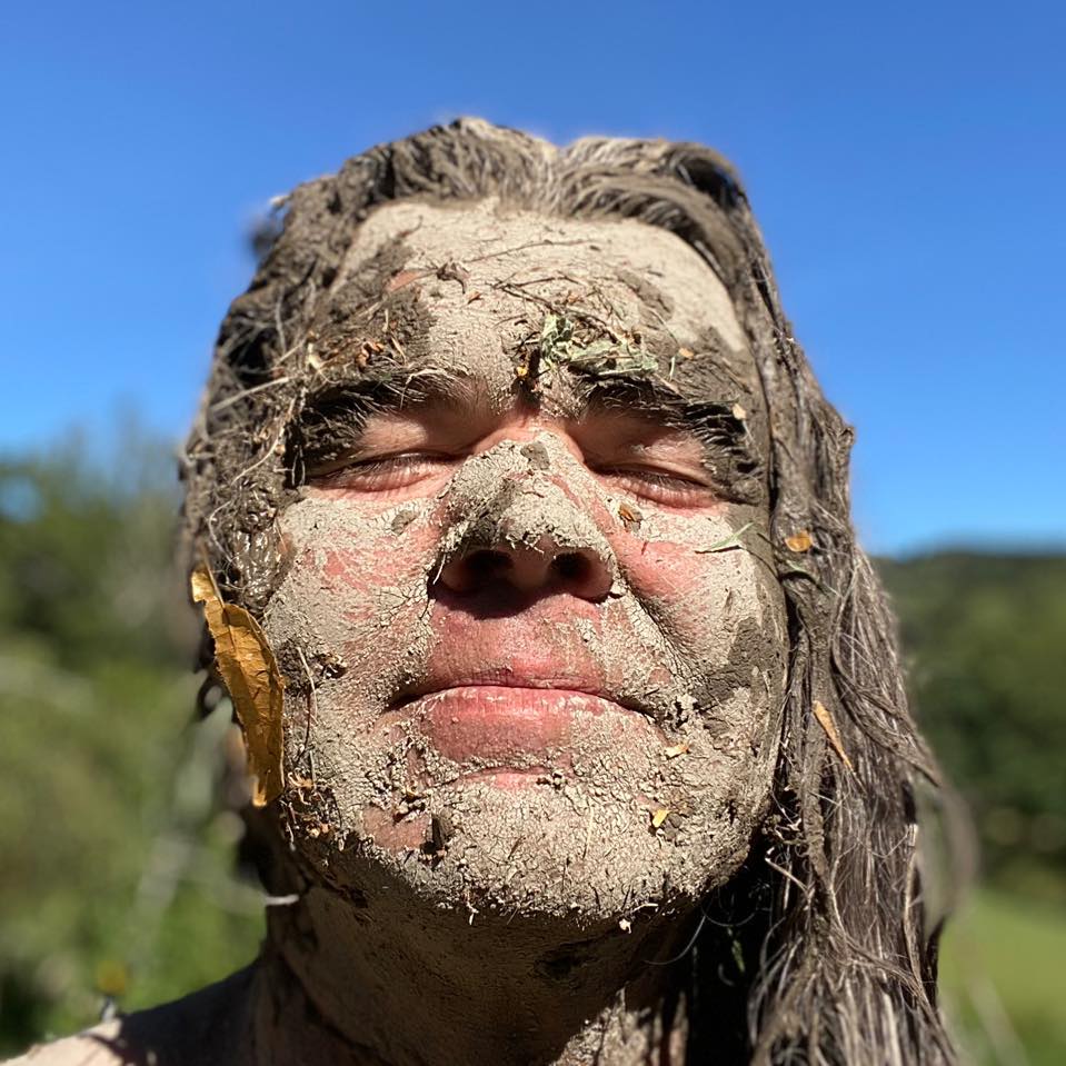 Portrait de Xavier Gaillot – créateur d’Exstatic Designs, visage enduit d’argile sacrée en immersion naturelle, entre art brut, tantra et reliance à la Terre.