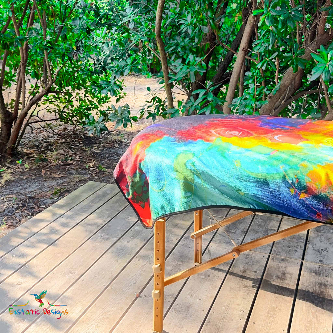 Détail de la serviette géante Tantra & Massage "L’Axe Sacré" sur une table de massage en extérieur, vue rapprochée de quelques chakras alignés et des couleurs arc-en-ciel, création énergétique de Xavier Gaillot.