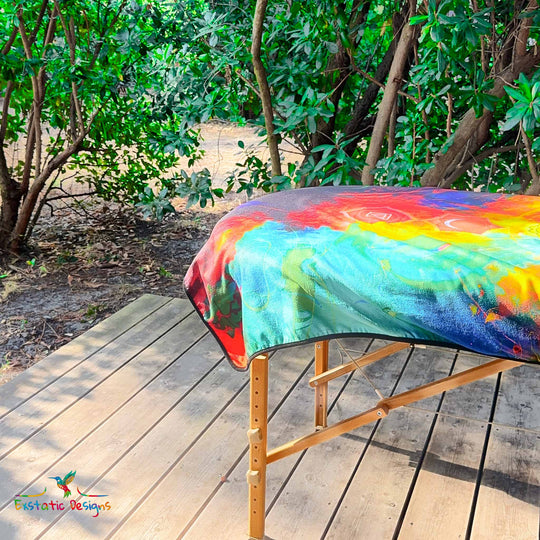 Détail de la serviette géante Tantra & Massage "L’Axe Sacré" sur une table de massage en extérieur, vue rapprochée de quelques chakras alignés et des couleurs arc-en-ciel, création énergétique de Xavier Gaillot.