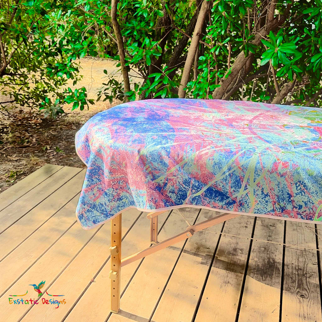 Détail de la serviette géante Tantra & Massage "Céleste Étreinte" sur une table de massage en extérieur, vue rapprochée des ailes angéliques et des couleurs violet-bleu, création vibratoire de Xavier Gaillot pour Exstatic Designs.