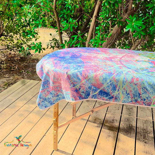 Détail de la serviette géante Tantra & Massage "Céleste Étreinte" sur une table de massage en extérieur, vue rapprochée des ailes angéliques et des couleurs violet-bleu, création vibratoire de Xavier Gaillot pour Exstatic Designs.