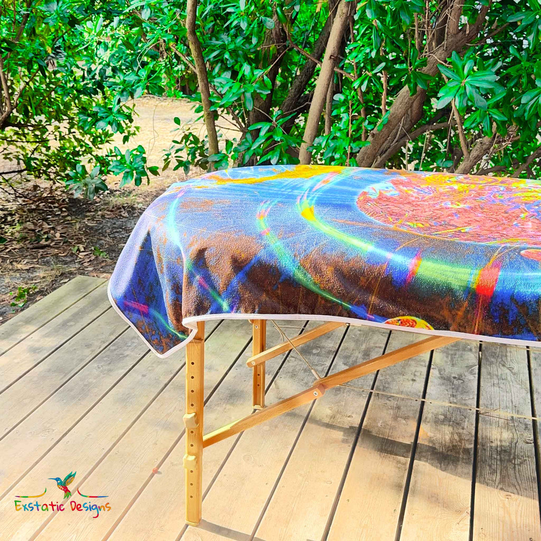 Détail de la serviette géante Tantra & Massage "La danse des sphères" sur une table de massage en extérieur, vue rapprochée des sphères lumineuses et des spirales dorées, création vibratoire de Xavier Gaillot.