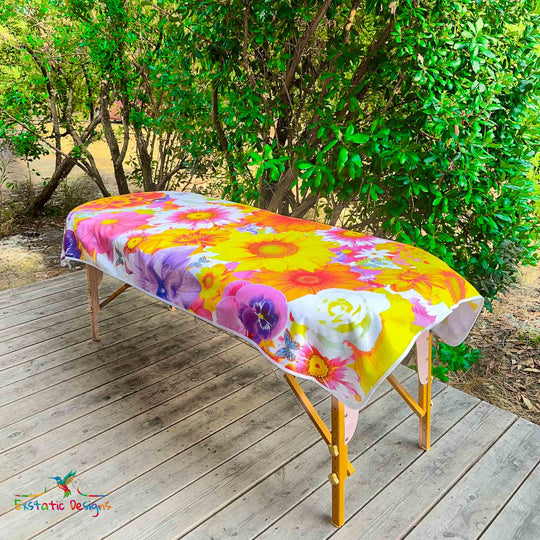 Serviette géante Tantra & Massage "Fleurs Libres" posée sur une table de massage en extérieur, vue complète, fleurs et papillons aux couleurs éclatantes, création vibratoire de Xavier Gaillot pour Exstatic Designs.