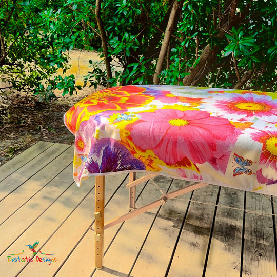 Détail de la serviette géante Tantra & Massage "Fleurs Libres" sur une table de massage en extérieur, vue rapprochée des fleurs et papillons colorés, création vibratoire de Xavier Gaillot pour Exstatic Designs.