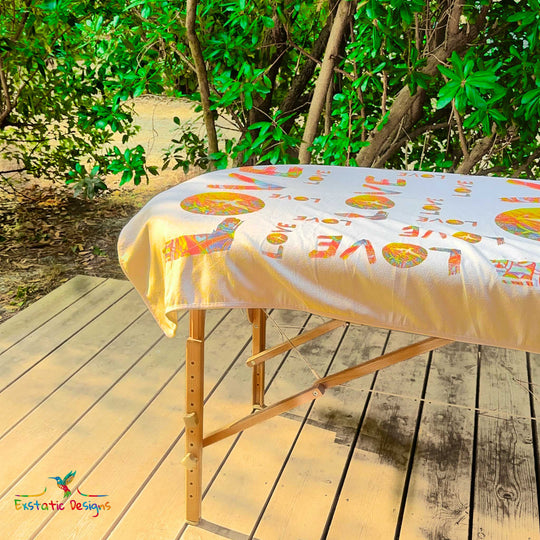 Détail de la serviette géante Tantra & Massage "L’Amour qui dégouline" sur une table de massage en extérieur, vue rapprochée des lettres LOVE et des mandalas solaires, création vibratoire de Xavier Gaillot.