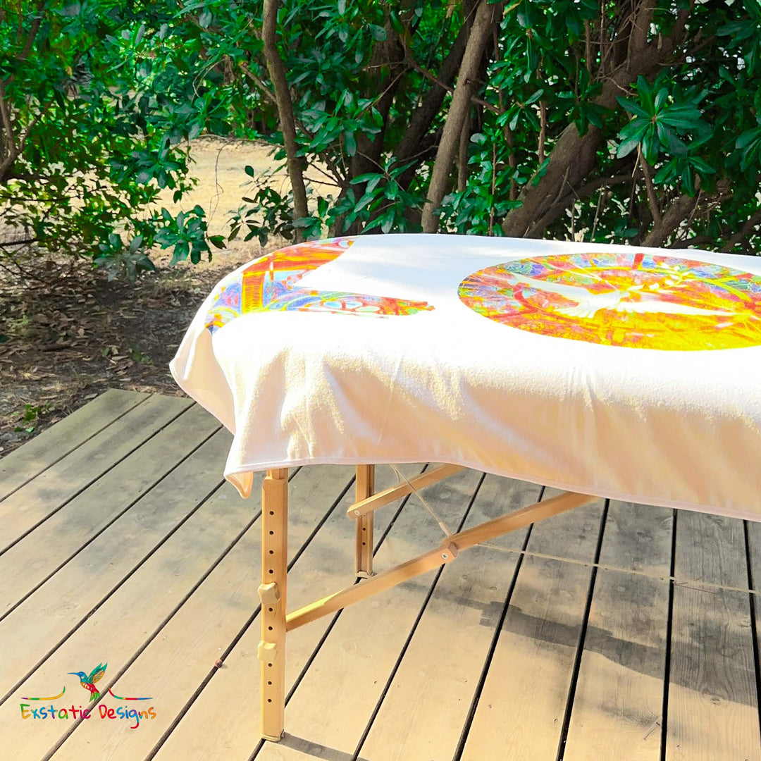 Détail de la serviette géante Tantra & Massage "L’Amour à Grande Échelle" sur une table de massage en extérieur, vue rapprochée du mot LOVE et du mandala lumineux, création vibratoire de Xavier Gaillot.