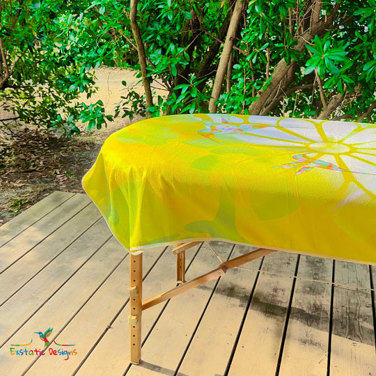 Détail de la serviette géante Tantra & Massage "Éclat de Grâce" sur une table de massage en extérieur, vue rapprochée des colibris et du lotus rayonnant, création spirituelle de Xavier Gaillot.