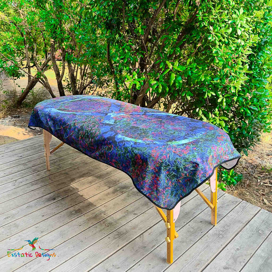 Serviette géante Tantra & Massage "Éternel instant" posée sur une table de massage en extérieur, vue complète, symbole infini bleu sur fond tellurique, création sacrée de Xavier Gaillot pour ancrage et présence.
