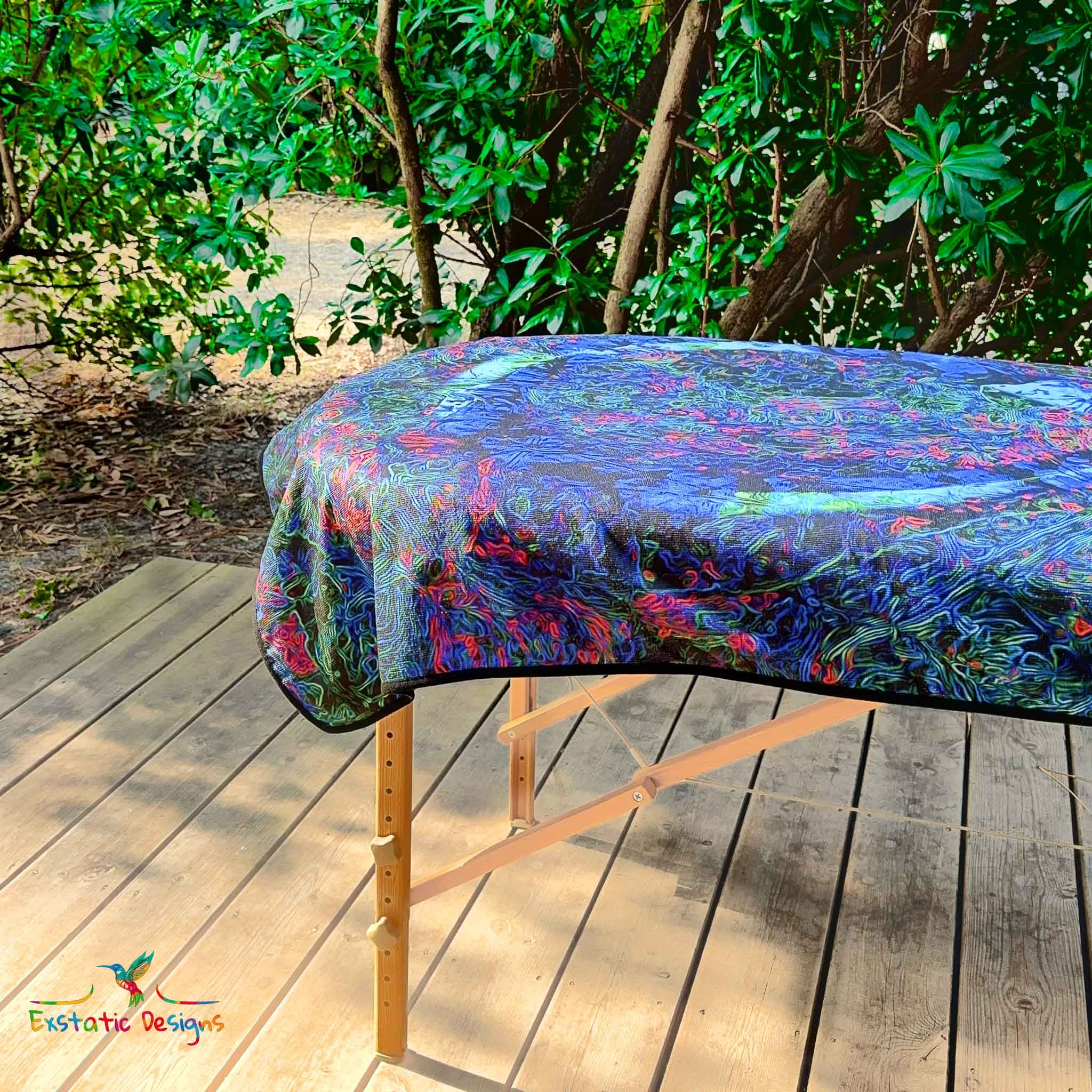 Détail de la serviette géante Tantra & Massage "Éternel instant" sur une table de massage en extérieur, vue rapprochée du motif infini bleu vibrant, création sacrée de Xavier Gaillot invitant à la présence.