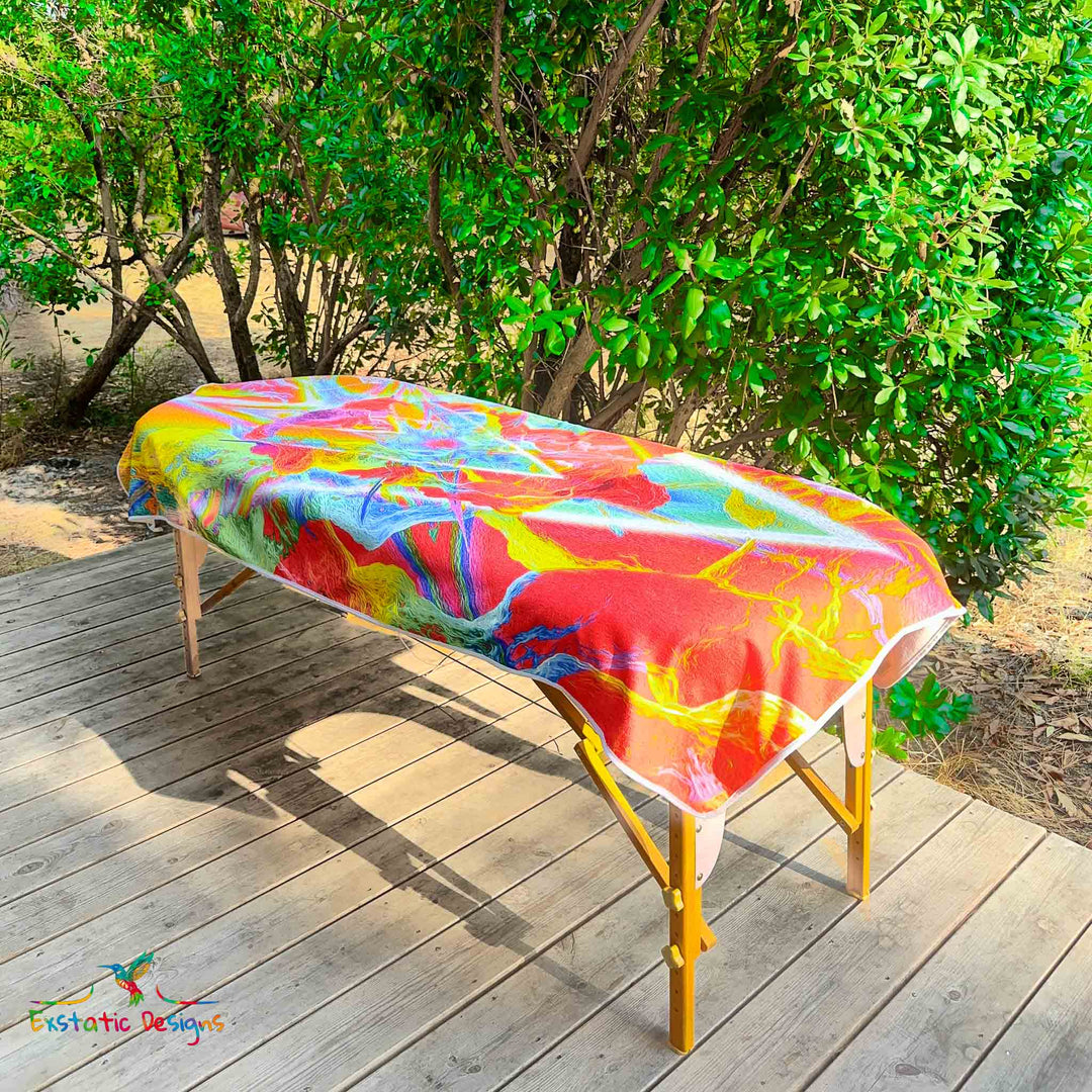 Serviette géante Tantra & Massage "Feu extatique" posée sur une table de massage en extérieur, vue complète, triangle inversé et feu sacré aux couleurs flamboyantes, création intense de Xavier Gaillot.