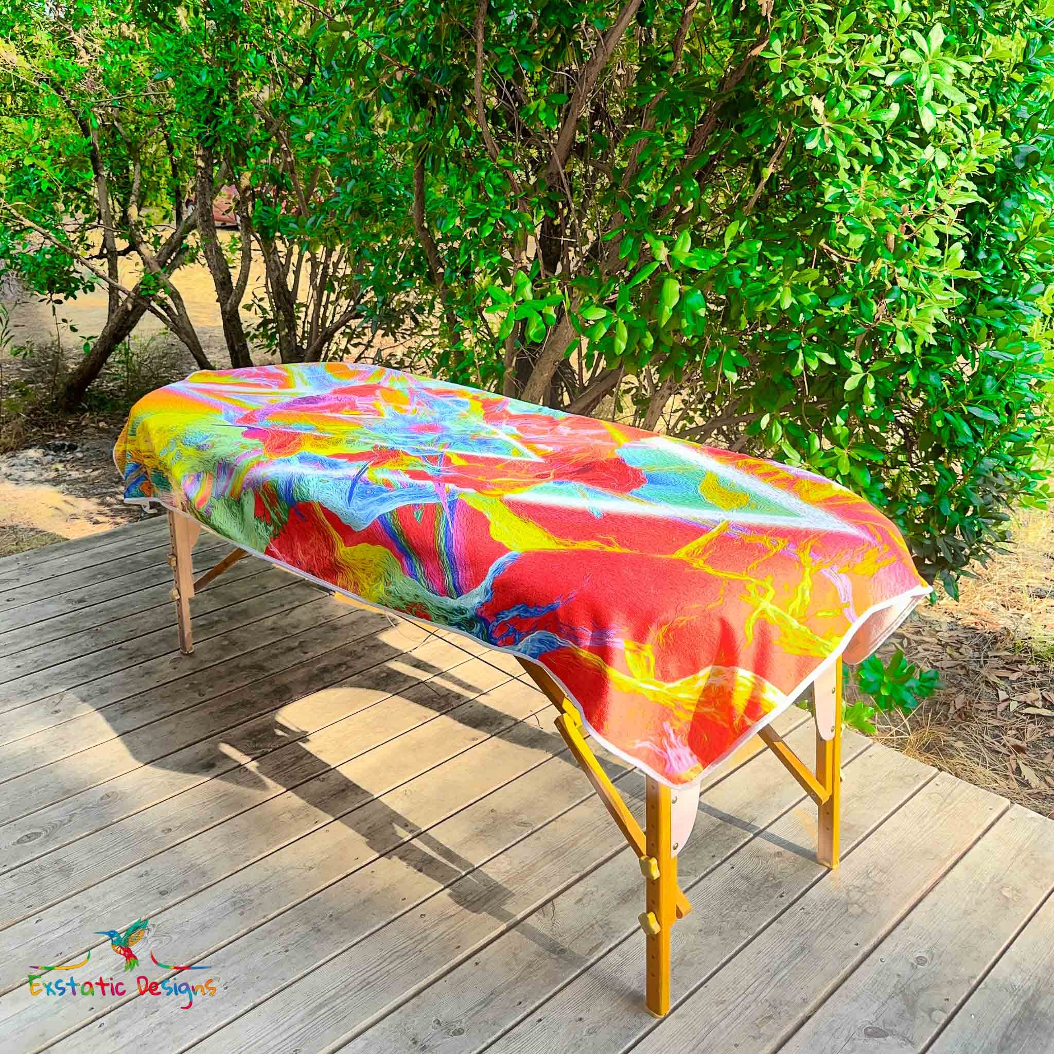 Serviette géante Tantra & Massage "Feu extatique" posée sur une table de massage en extérieur, vue complète, triangle inversé et feu sacré aux couleurs flamboyantes, création intense de Xavier Gaillot.