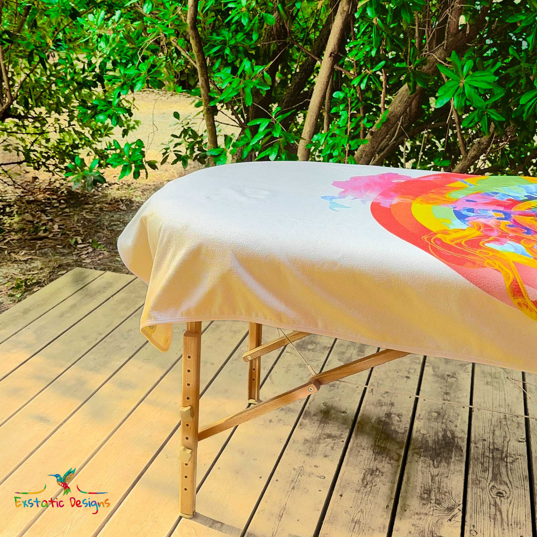 Détail de la serviette géante Tantra & Massage "Shiva danse" sur une table de massage en extérieur, vue rapprochée du motif central et des volutes colorées, création spirituelle de Xavier Gaillot.