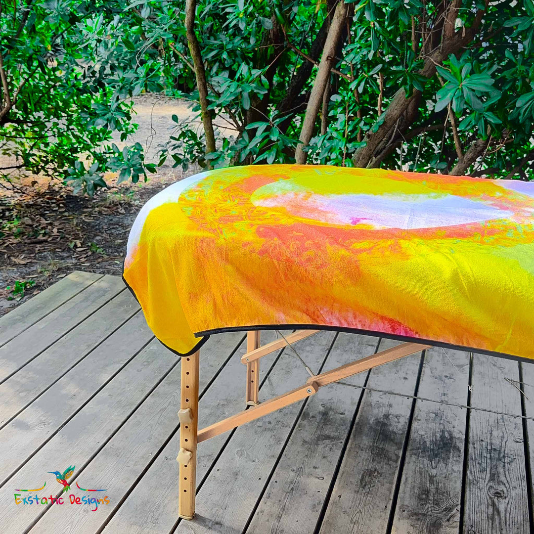Détail de la serviette géante Tantra & Massage "Le Souffle de l’Infini" sur une table de massage en extérieur, vue rapprochée du symbole infini et des couleurs vibrantes, création spirituelle de Xavier Gaillot.