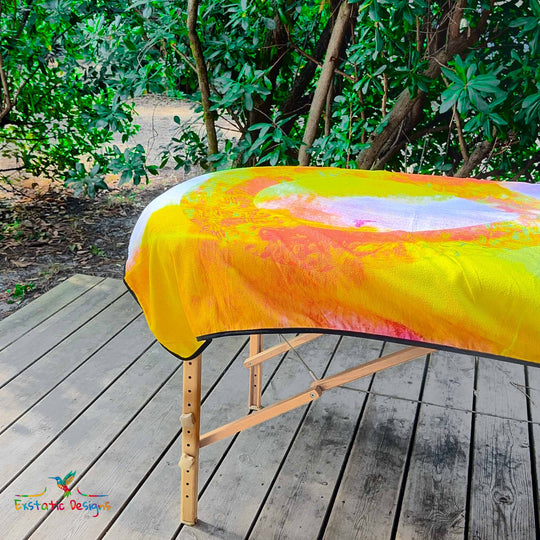 Détail de la serviette géante Tantra & Massage "Le Souffle de l’Infini" sur une table de massage en extérieur, vue rapprochée du symbole infini et des couleurs vibrantes, création spirituelle de Xavier Gaillot.